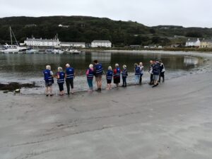 Image show participants in the 2021 SÚIL Lines of Longitude sculptural sensory walk on the beach in the harbour of Rathlin Island off the Antrim coast.